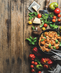 Italian pasta spaghetti with tomato sauce and meatballs in cast iron pan served with Parmesan cheese, fresh basil and colorful tomatoes over old rustic wooden background. Top view, copy space
