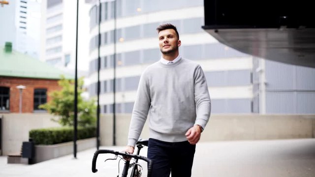 young man walking along city street with bicycle