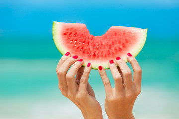 Hand holding slice of watermelon on the beach. 