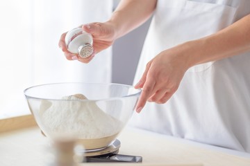 Woman adding salt to flour.