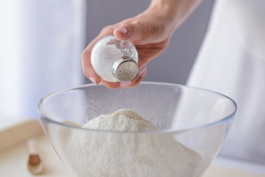 Woman adding salt to flour.