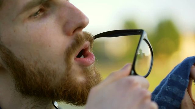 Tourist wearing hat and cleaning his glasses by using tissue
