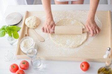Woman rolling pizza dough using rolling pin.