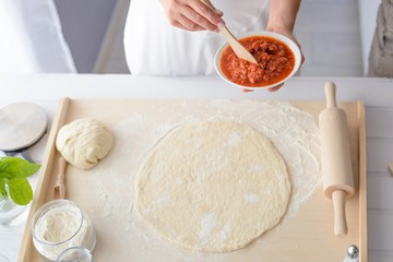 Woman adding tomato sauce on pizza
