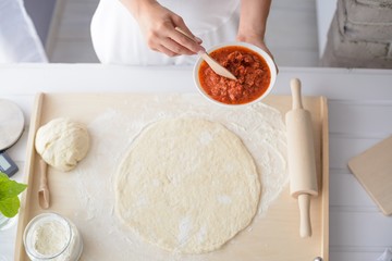 Woman adding tomato sauce on pizza