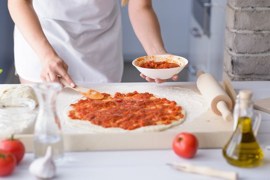 Woman adding tomato sauce on pizza
