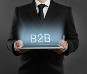 B2B business to business concept. Businessman with tablet on grey background