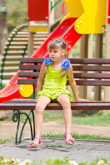 Upset girl sitting on the bench on the background of the playground