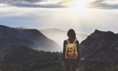 Hipster young girl with bright backpack enjoying sunset on peak of foggy mountain. Tourist traveler on background valley landscape view mockup. Hiker looking sunlight flare in trip in northern spain - obrazy, fototapety, plakaty