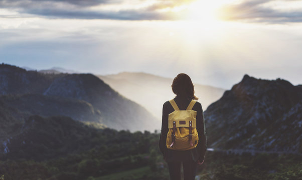 Hipster young girl with bright backpack enjoying sunset on peak of foggy mountain. Tourist traveler on background valley landscape view mockup. Hiker looking sunlight flare in trip in northern spain
