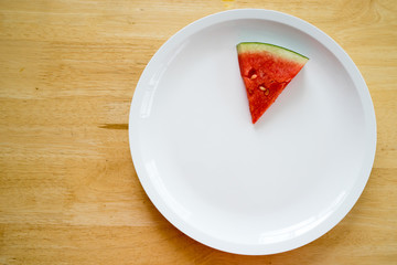 Watermelon slice on a white plate on a wood background, Top view