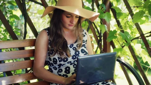 Girl using laptop in the arbor and smiling to the camera
