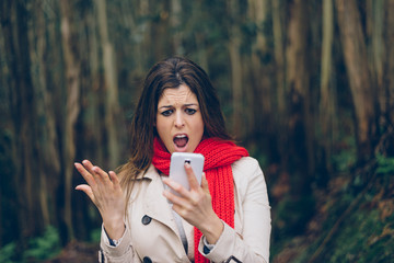 Upset woman looking worried about losing mobile or gps signal coverage on smartphone. Angry brunette girl in trouble or receiving bad news during autumn trip.