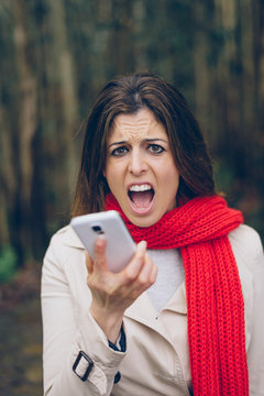 Upset woman shouting and looking worried about losing mobile or gps signal coverage on smartphone. Angry brunette girl in trouble or receiving bad news during autumn trip.