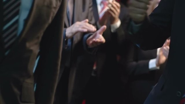 Slow motion mid-section shot of two politicians shaking hands before applauding public, then walking towards camera