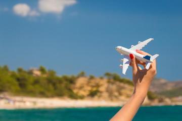 Close up of female hand holding white airplane toy model against the beautiful beach and sky.