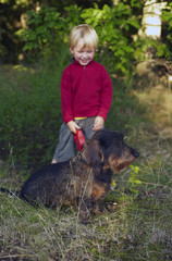 Cute little boy with dog (dachshund) in the woods.

