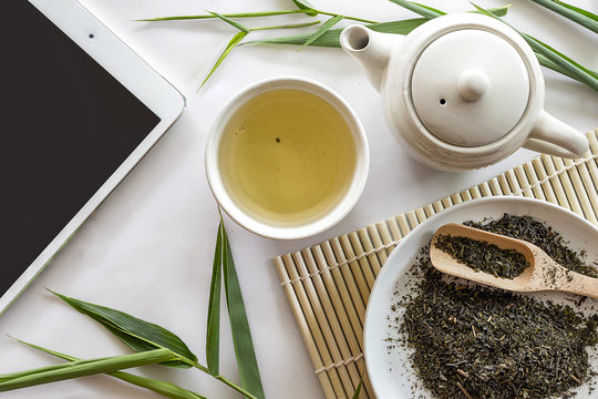 tablet computer, teapot and cup of herbal green tea on bamboo with white table background. over light