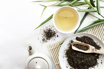 teapot and cup of herbal green tea on bamboo with white table background. over light