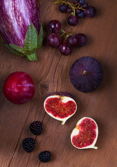 Ripe purple figs, plums, grape, eggplant and onion. Fruit and vegetable still life on wooden background. Clean eating concept. Colorful food collage. View from above, top studio shot