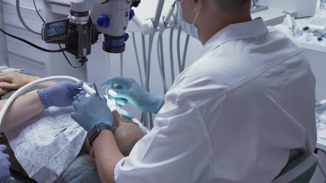 Male dentist receiving the root canals of the patient using the microscope.
