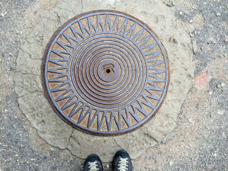 Women legs standing at iron hatch on pavement street