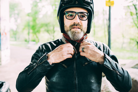 Mature male motorcyclist wearing eyeglasses fastening leather jacket