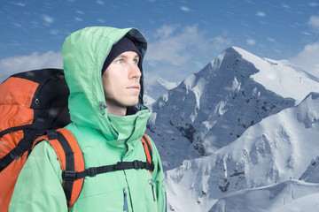 The mountaineer looks at the peak, standing against a winter mountain landscape.