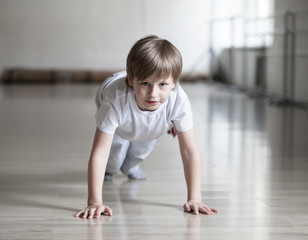 Cute boy in white clothes practicing capoeira (brazilian martial art that combines elements of dance, acrobatics and music)  in gym
