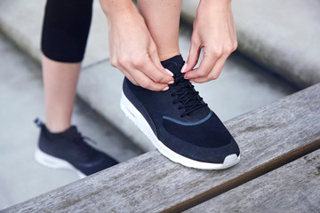 Close up of woman with foot raised on bench tying shoelace