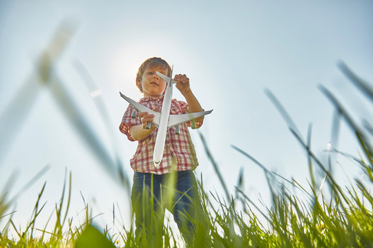 Low angle view of boy standing in grass checking toy airplane tail