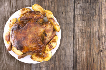 Whole roasted chicken with potatoes on rustic wooden table. Sele