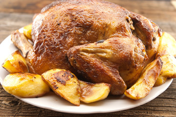 Whole roasted chicken with potatoes on rustic wooden table. Sele