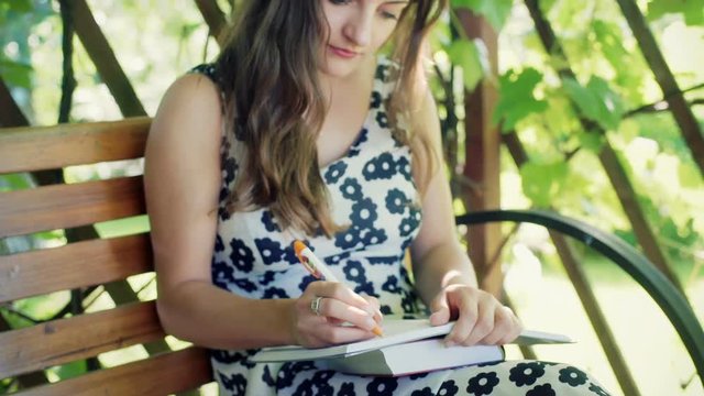 Absorbed girl sitting in the arbor and writing thoughts in her notebook
