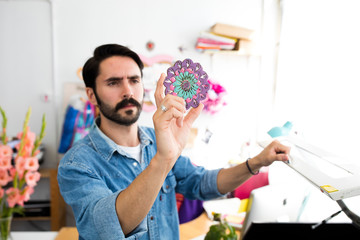 Young male designer holding up circular print in printing press studio