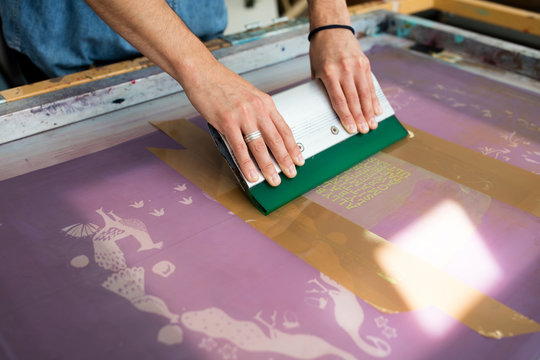 Hands of young male printer using squeegee in printing press studio