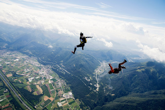 Freestyle skydiving team training together. One man  performing air-ballet, another jumper is filming with video camera on helmet, Locarno, Tessin, Switzerland
