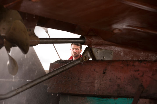 Male ship painter using pressure washer to clean ship hull