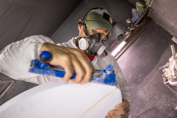 Male carpenter using carpentry equipment on surfboard in surfboard maker's workshop