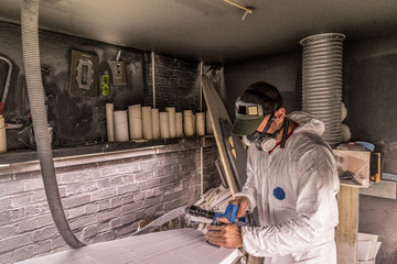 Male carpenter using carpentry equipment on surfboard in surfboard maker's workshop