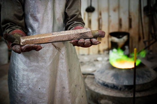 Mid section of male foundry worker holding bronze ingot in bronze foundry