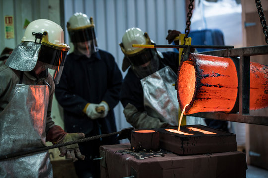 Male foundry workers pouring bronze melting pot in bronze foundry