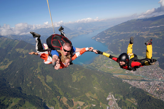 Smiling tandem sky divers holding hand with free faller, Interlaken, Berne, Switzerland