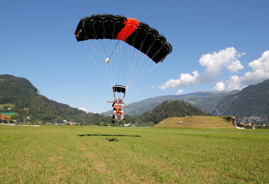 Tandem sky divers landing in field with parachute, Interlaken, Berne, Switzerland