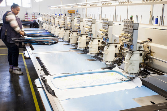 Female factory worker preparing cloth for speed stitching  programmed embroidery machine in clothing factory