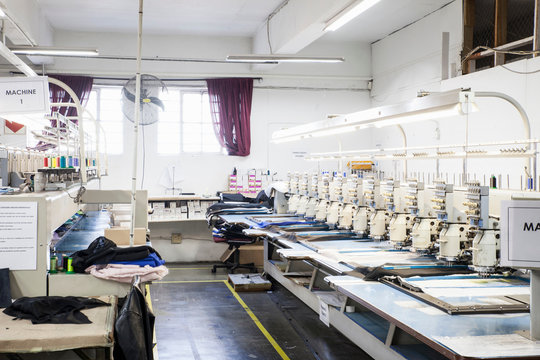 Rows of programmed embroidery machines speed stitching  cloth in clothing factory