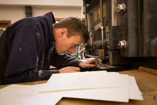 Young male printer preparing printing machinery in printing press workshop