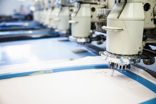 Rows of programmed embroidery machines speed stitching white cloth in clothing factory