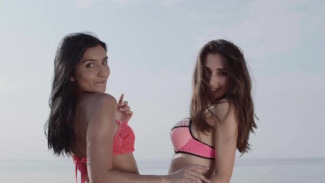 Two girls in bikini turn into camera, smile and wave their perfect hair