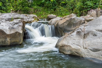 Fototapeta na wymiar Waterfall cascades flowing over flat rocks in forest.